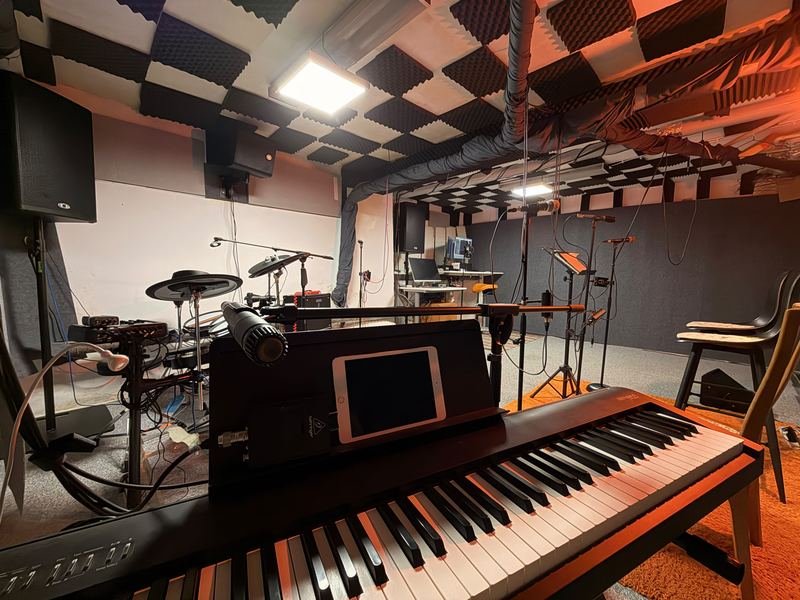 Pohľad cez digitálne piano Roland na elektronické bicie, akustický strop a nahrávacie pracovisko v pozadí