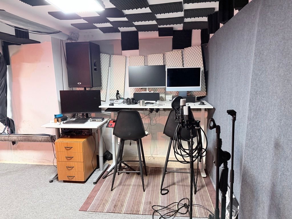 Nahrávacie pracovisko: biely stôl s dvoma monitormi, modrý iMac a mikrofón s pop filtrom